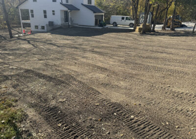 Freshly graded earth with two story residential structure, skid steer and van in background