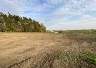 Freshly graded earth with tree line and fencing on perimeter.